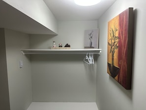 Une pièce avec un plafond blanc, une étagère ornée d’une pancarte de bienvenue, un tableau encadré et une plante en pot.