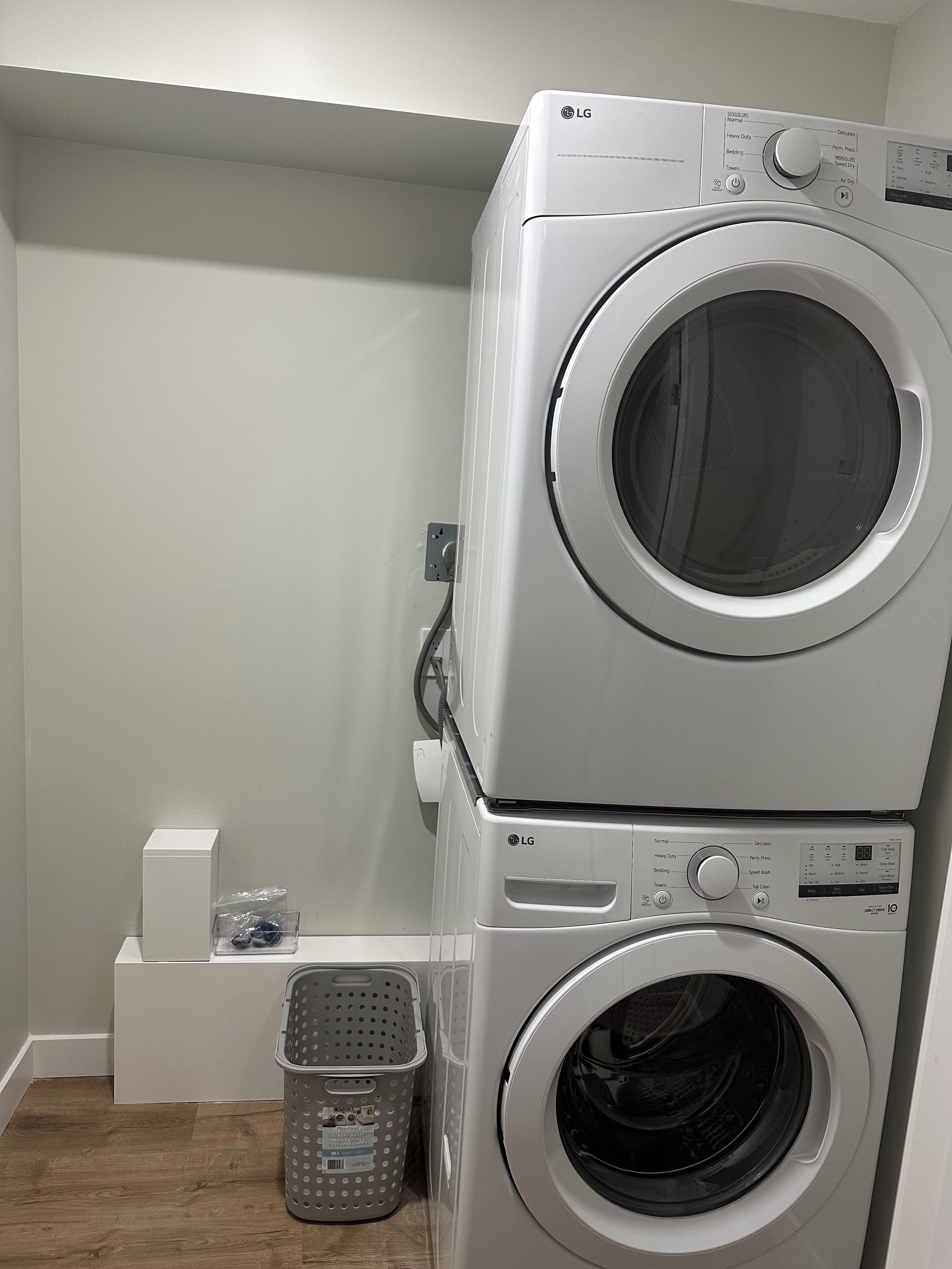 Een gestapelde wasmachine en droger met bedieningspanelen, een stopcontact en een wasmand.