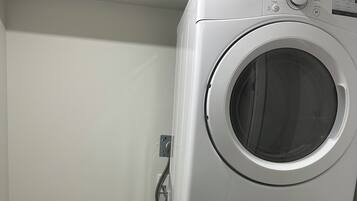 Een gestapelde wasmachine en droger met bedieningspanelen, een stopcontact en een wasmand.