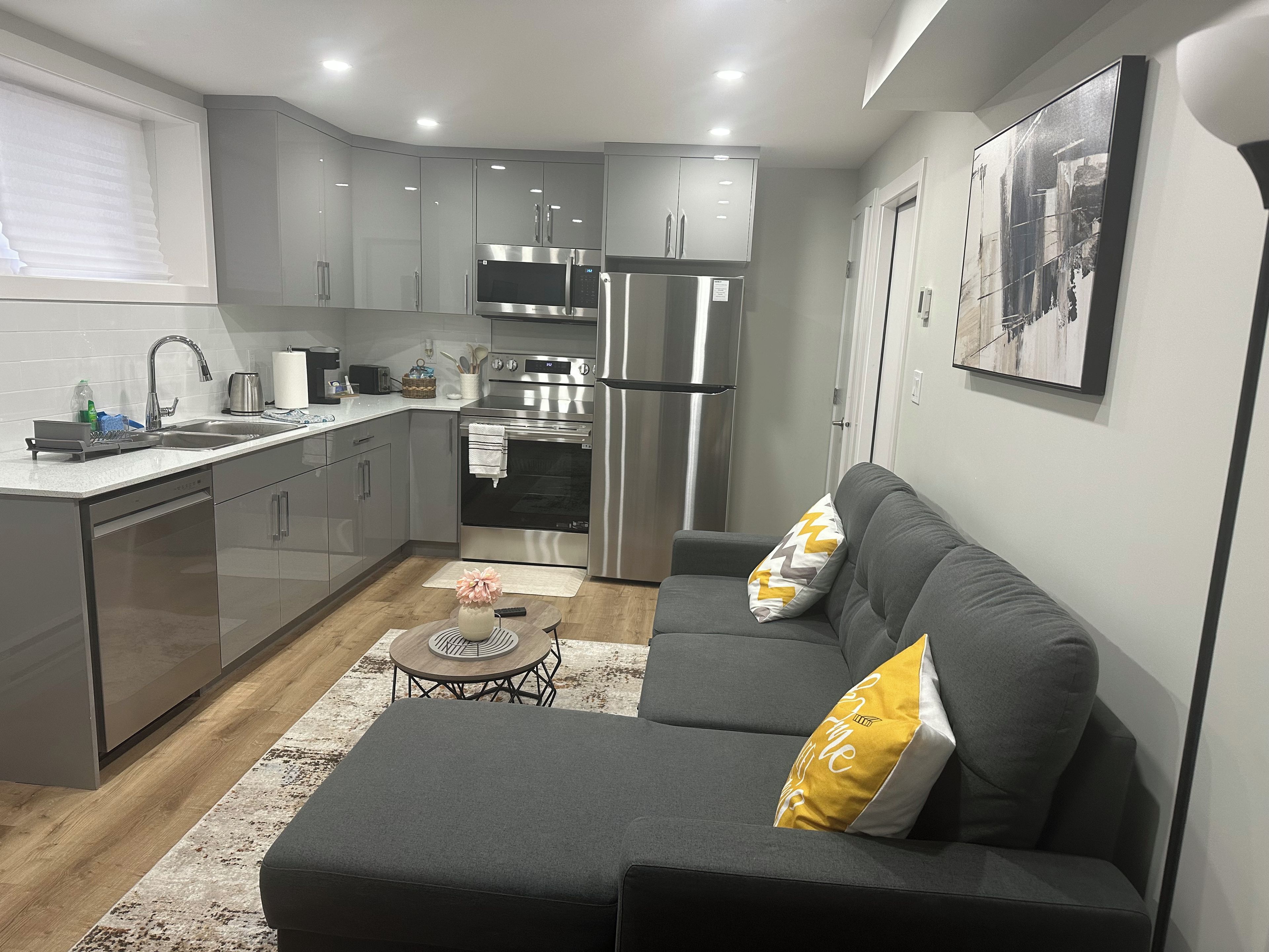 A modern kitchen with stainless steel appliances, a grey sofa with cushions, and a small round table with a vase.