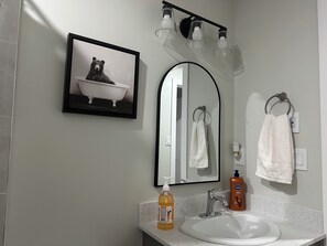 Een badkamer met een witte wasbak, een lijst met een foto van een beer in bad, een spiegel en drie lampen boven de spiegel.