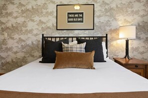 A neatly made bed with a brown pillow, a framed sign above it, and a nightstand with a lamp to the right. - Ski, Hike, Soak: The Alpine Escape Awaits (Steamboat Springs)