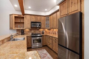 A kitchen with wooden cabinets, a stainless steel refrigerator, a microwave, a stove, and a sink. - Ski, Hike, Soak: The Alpine Escape Awaits (Steamboat Springs)