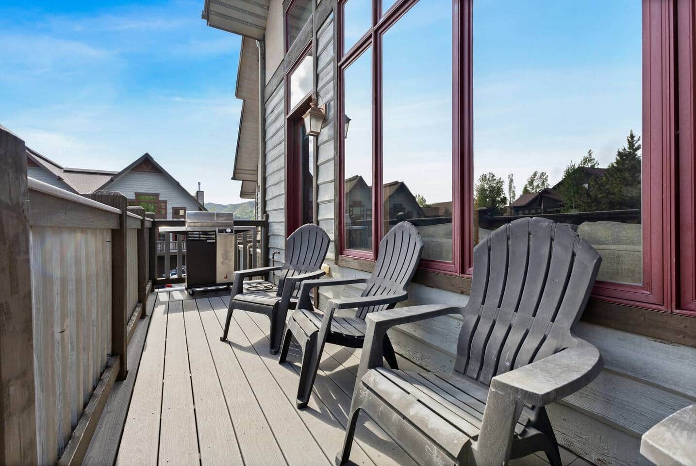A wooden deck with Adirondack chairs and a grill, overlooking a residential area.