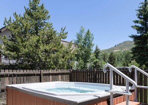 A hot tub with a wooden deck and metal railings, surrounded by a wooden fence and trees. - Ski, Hike, Soak: The Alpine Escape Awaits (Steamboat Springs)