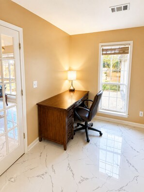 A room with a wooden desk, a chair, a lamp, a window, and a door.