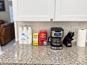 A kitchen counter with a coffee maker, a box of Folgers coffee, a carton of Domino granulated sugar, and a stack of foam cups. - Pool table and sports home (Montgomery)