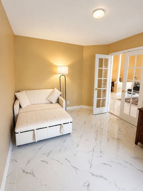 A bedroom with a bed, a floor lamp, and a door leading to another room.