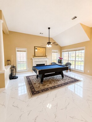 A spacious room with a pool table, a fireplace, and large windows.