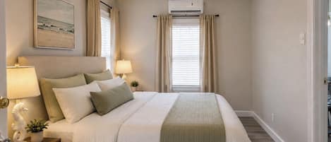 A bedroom with a bed, two bedside lamps, a ceiling fan, an air conditioning unit, and a window with curtains.