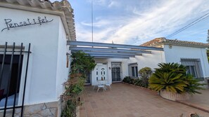 Ein Gebäude mit weißer Fassade, einer überdachten Terrasse mit Tisch und Stühlen sowie einem Schild mit der Aufschrift 'Pensativo'.