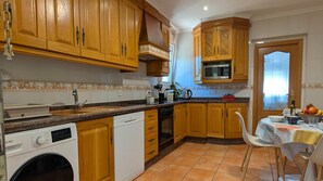 Cozinha com armários de madeira, micro-ondas embutido, máquina de lavar e espaço de jantar com mesa posta para dois.
