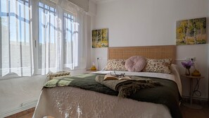 Een slaapkamer met een groot bed, een hoofdbord, een nachtkastje, een lamp en twee schilderijen aan de muur.