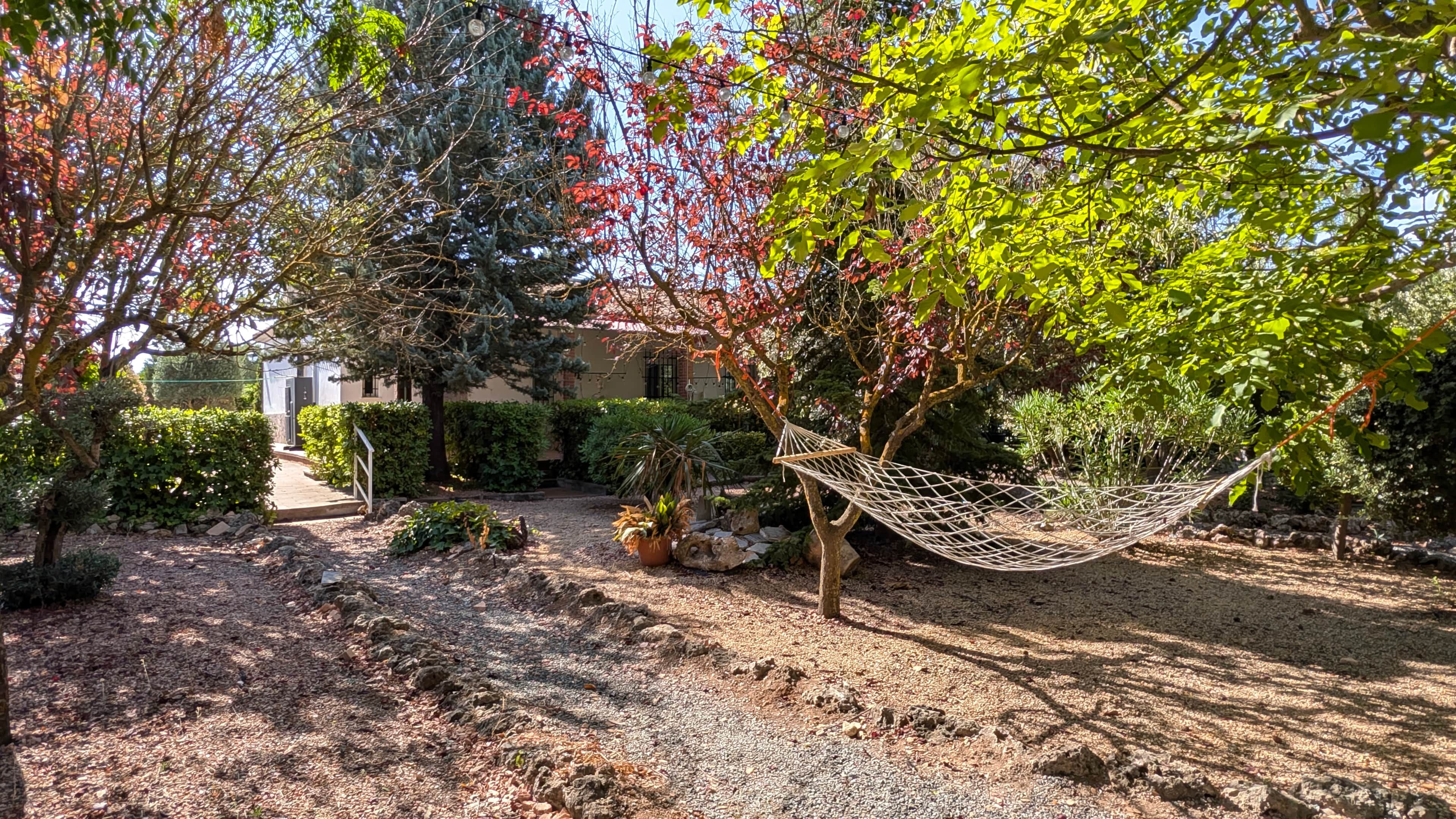 Un jardín con una hamaca, árboles y un edificio al fondo.