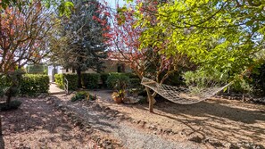 Un jardin avec un hamac, des arbres et un bâtiment en arrière-plan.