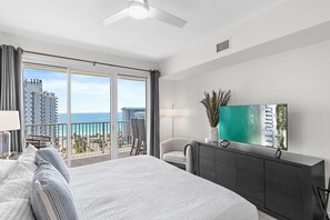 Ein Hotelzimmer mit einem großen Bett, einem Fernseher, einem Balkon mit Meerblick und Stadtansicht.