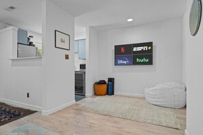 Un saló modern amb un televisor de pantalla plana que mostra serveis de streaming, una zona de cuina al fons i una zona d'estar acollidora amb un seient de forma de greu.