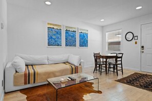 A living room with a sofa, a glass coffee table, a dining table with chairs, and artwork on the wall. - Chic Clarksville Condo w/ Covered Patio & Gated Keypad Entry - Near Downtown (Austin)