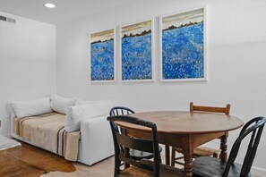 A dining area with a round wooden table and four chairs, a white sofa with a striped blanket, and three framed paintings on the wall. - Chic Clarksville Condo w/ Covered Patio & Gated Keypad Entry - Near Downtown (Austin)
