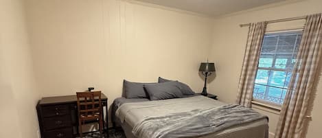 A bedroom with a bed, a nightstand, a lamp, a dresser, and a window with curtains.