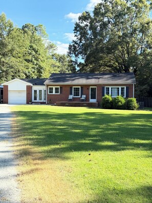 A single-story house with a garage, a front porch with two chairs, and a well-maintained lawn. - Spacious 4-bedroom house in Graham: Hot tub, Pool, Dog-friendly w/fenced yard (Graham)