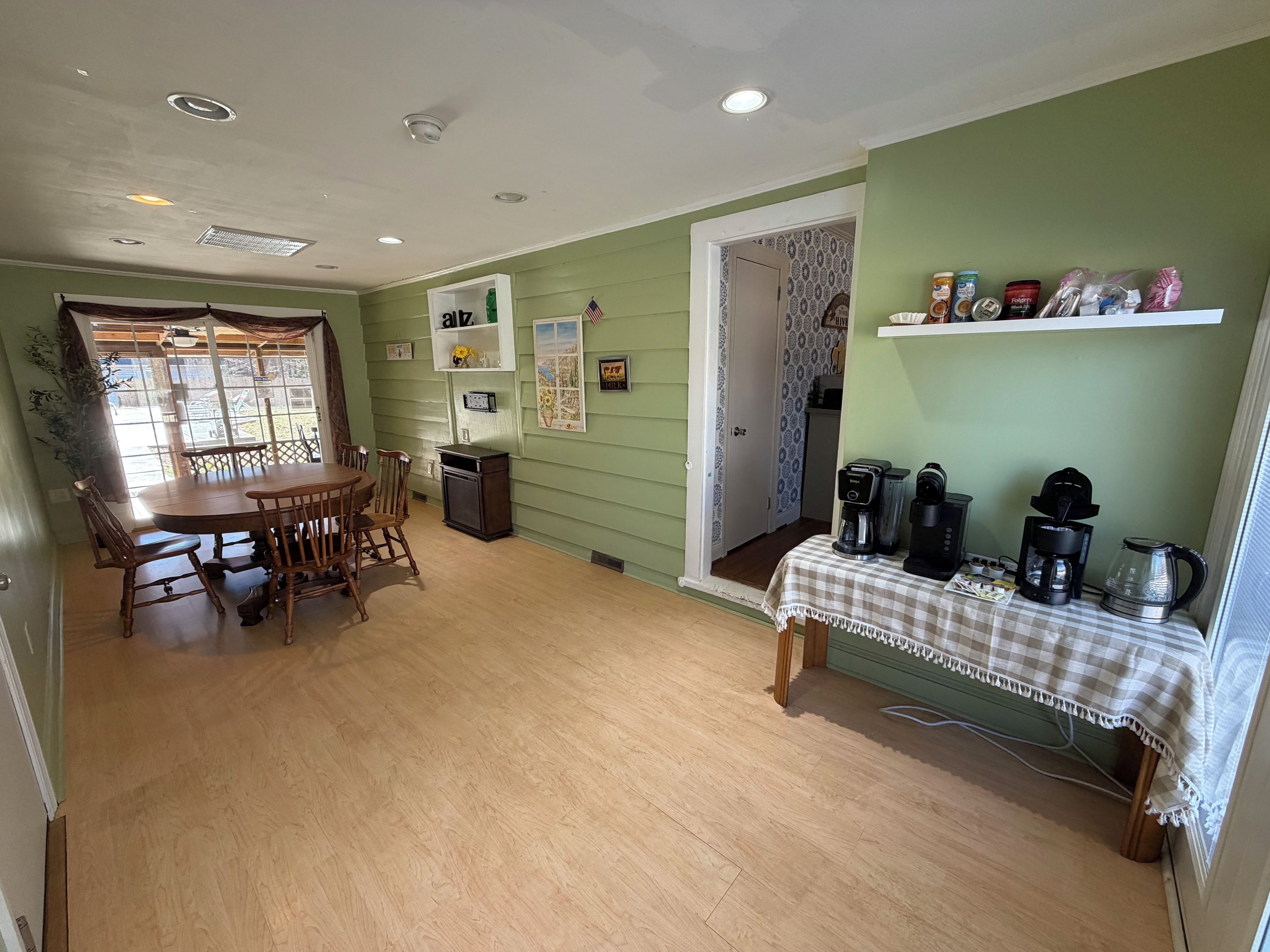 A dining area with a wooden table and chairs, a small trash bin, and a coffee station with multiple coffee makers and a kettle.