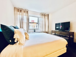 A hotel room with a bed, a TV, and a window with curtains. - Midtown East Oversized Studio (New York)