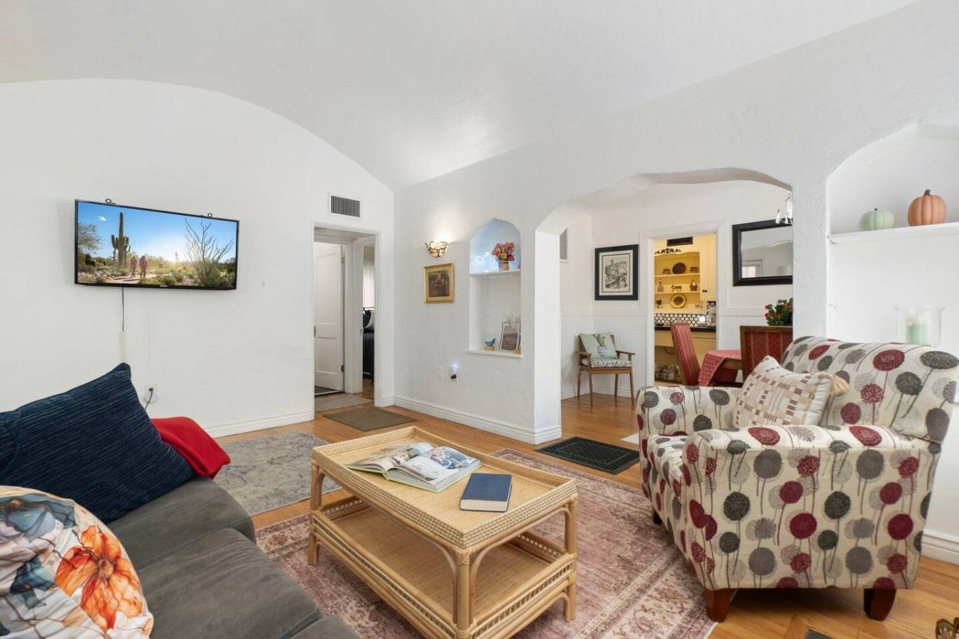 A living room with a sofa, armchair, coffee table, and a television mounted on the wall.