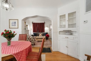 Ein Essbereich mit einem Tisch für zwei Personen, einem Sofa im Hintergrund und einem weißen Schrank mit Glastüren.
