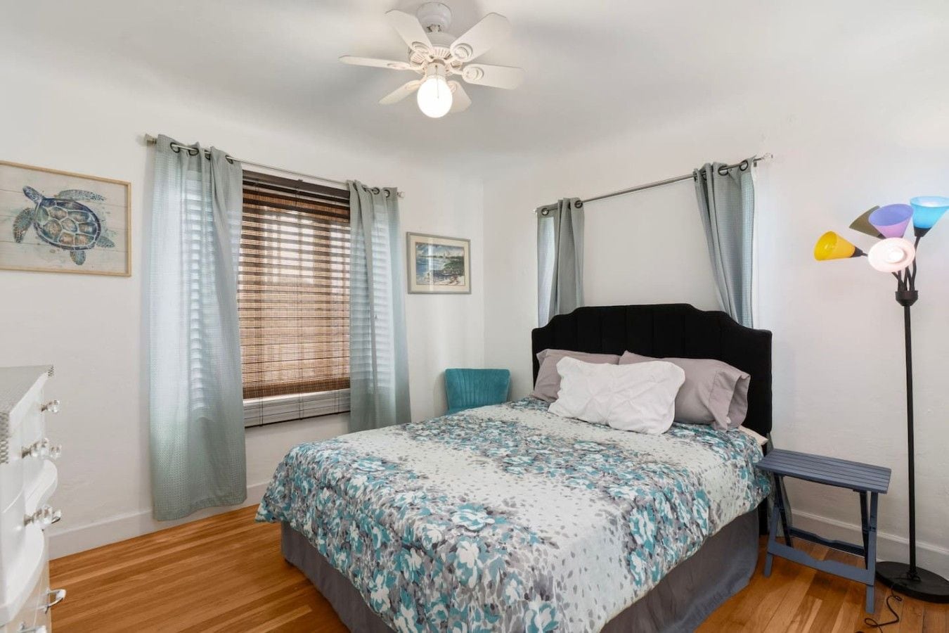 A bedroom with a bed, a ceiling fan, a window with blinds, and a bedside lamp.