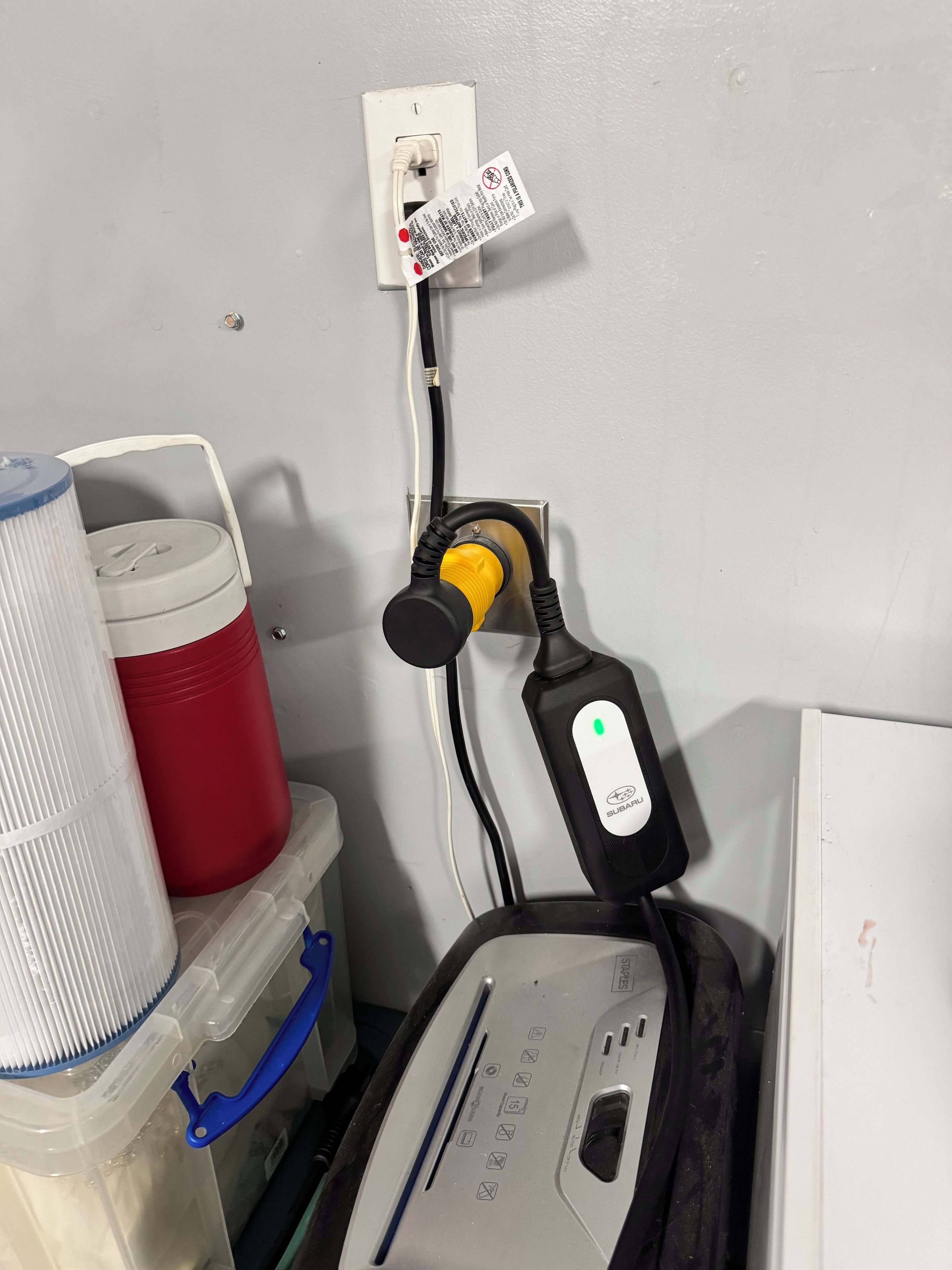 Un enchufe con un tapón, una regleta y un recipiente rojo.