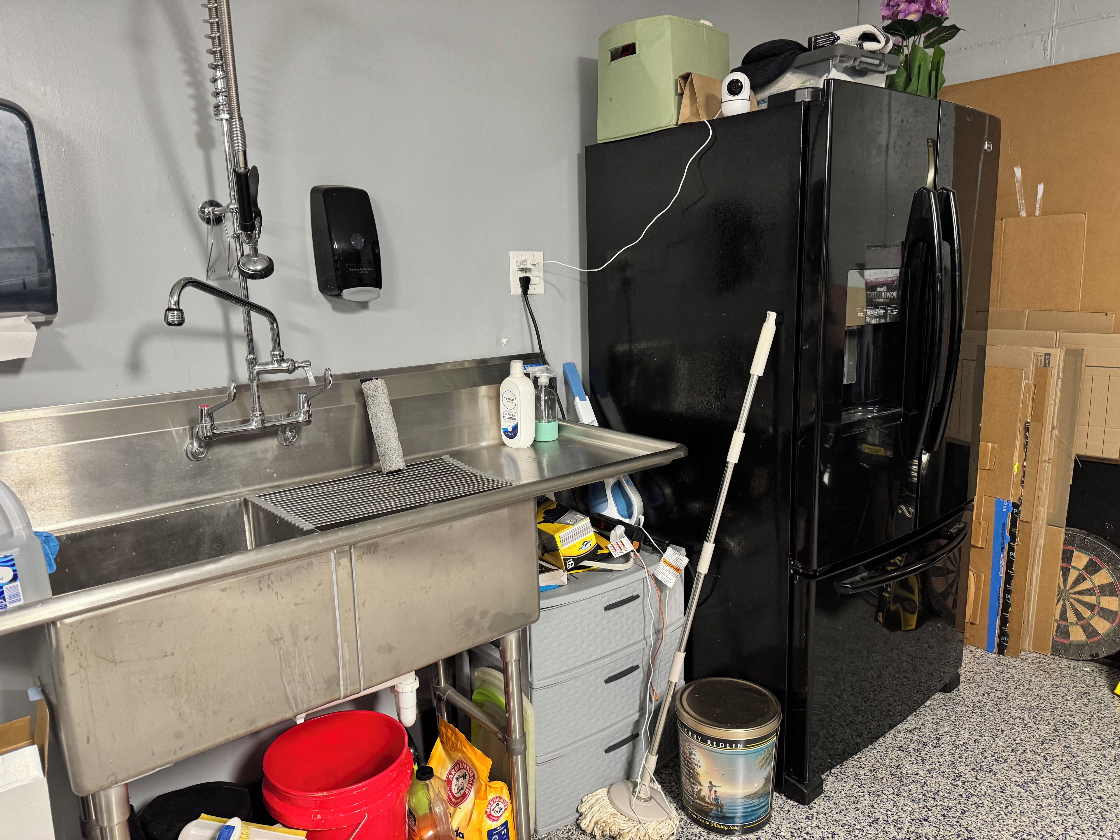 A kitchen with a stainless steel sink, a black refrigerator, and a red bucket.