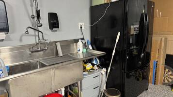 A kitchen with a stainless steel sink, a black refrigerator, and a red bucket.