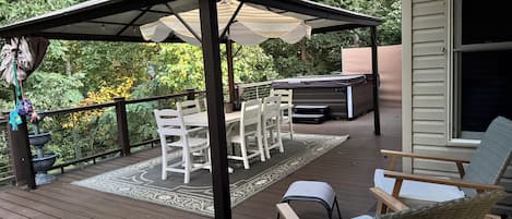 Una terraza cubierta al aire libre con mesa y sillas, un jacuzzi y una pérgola que da sombra.
