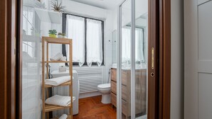 Un bagno moderno con ripiano in legno, piastrelle bianche, un water e box doccia in vetro.