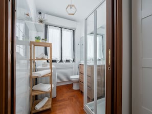 Een moderne badkamer met een houten plank, witte tegels, een toilet en een douchecabine met glazen wanden.