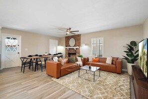 A living room with a fireplace, a ceiling fan, a dining area with a table and chairs, and a large plant. - Glendale Retreat Spacious Yard & RV Parking (Glendale)