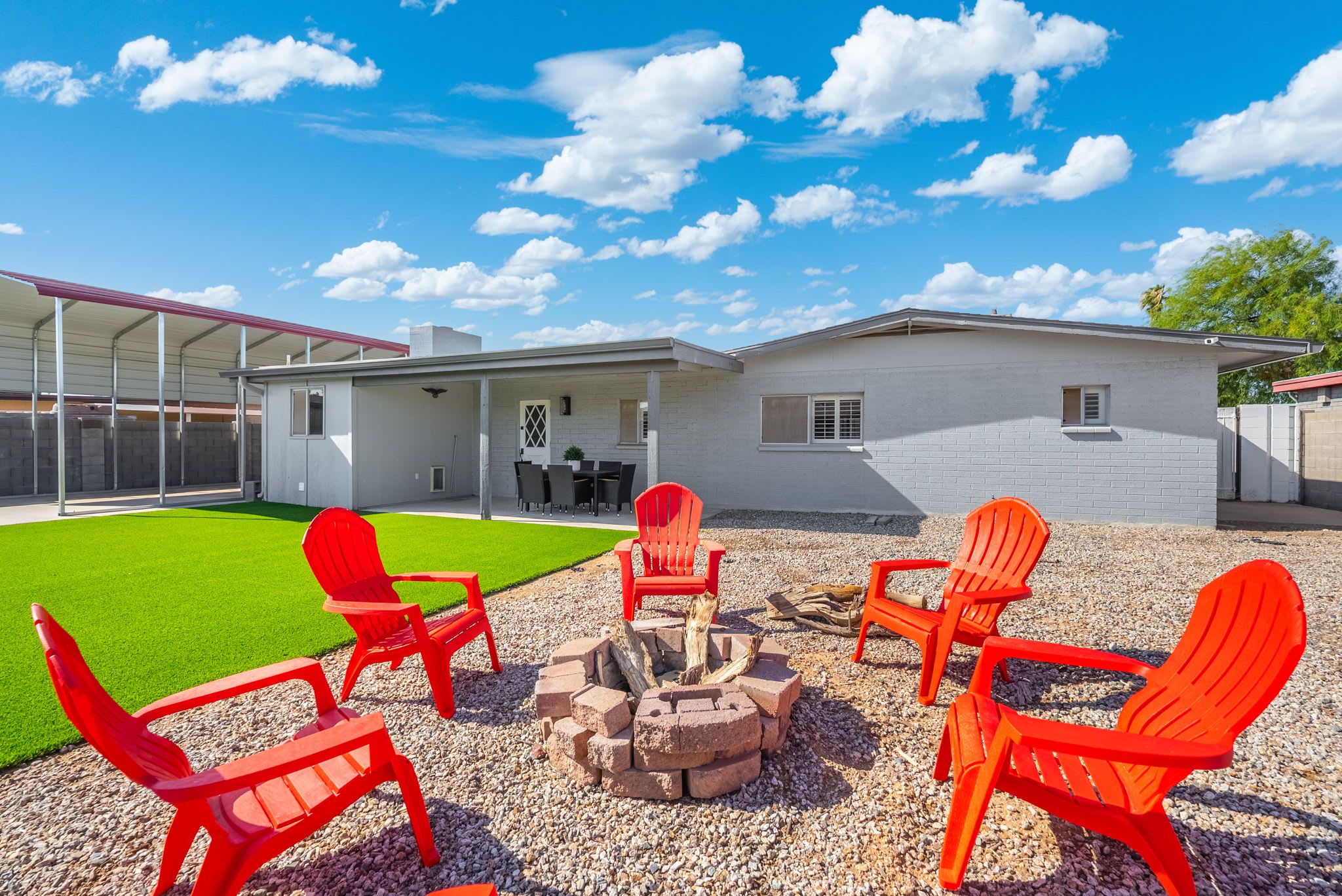 A house with a covered patio, outdoor seating area with red chairs, and a fire pit.