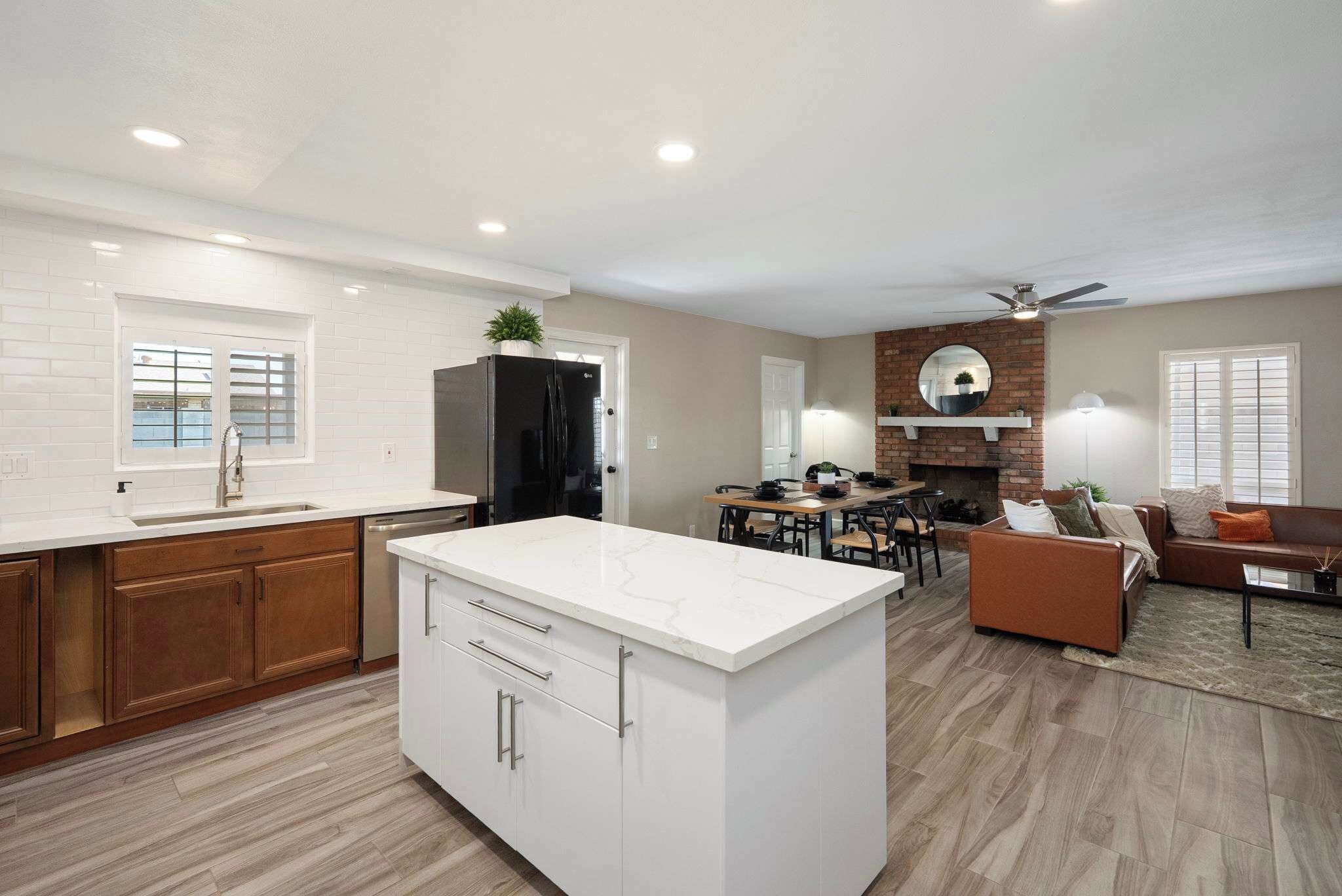 Una cocina moderna con armarios blancos, una isla central y una zona de comedor con chimenea de ladrillo.