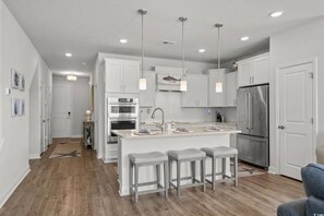 A modern kitchen with white cabinets, stainless steel appliances, and a central island with bar stools. - Barefoot Resort Getaway | Golf, Pool & Beach (North Myrtle Beach)