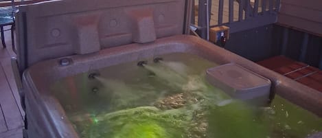 Ein Whirlpool mit einer hölzernen Sitzbank, umgeben von einer Terrasse mit Geländern und Lichterketten.