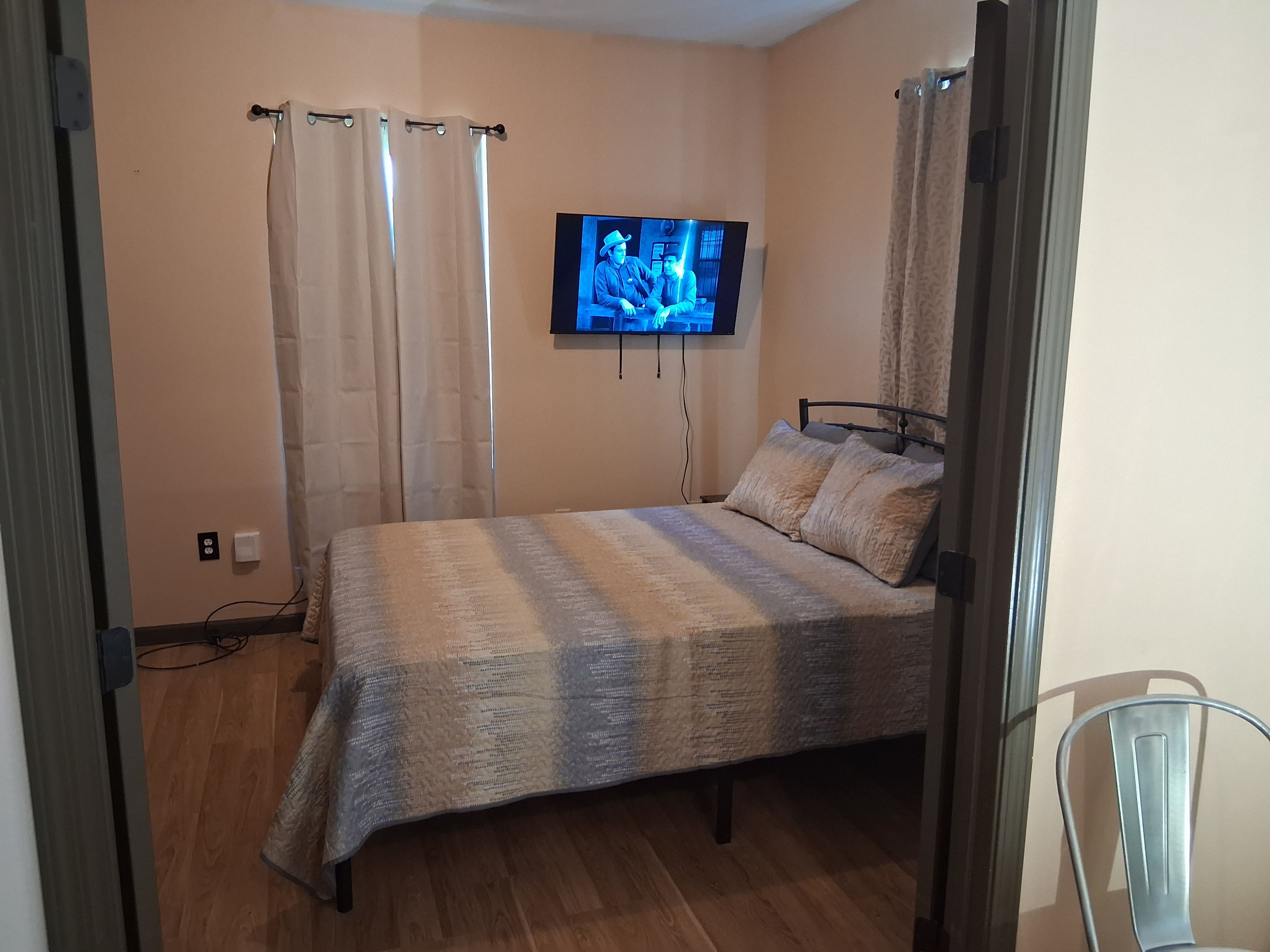 Ein Schlafzimmer mit einem Bett, Vorhängen, einem Fernseher und einem Sessel.