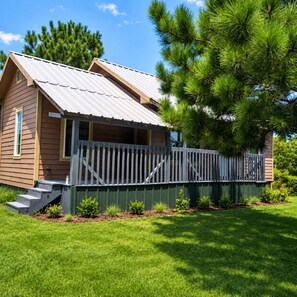 A wooden cabin with a metal roof, a porch, and a fenced yard.