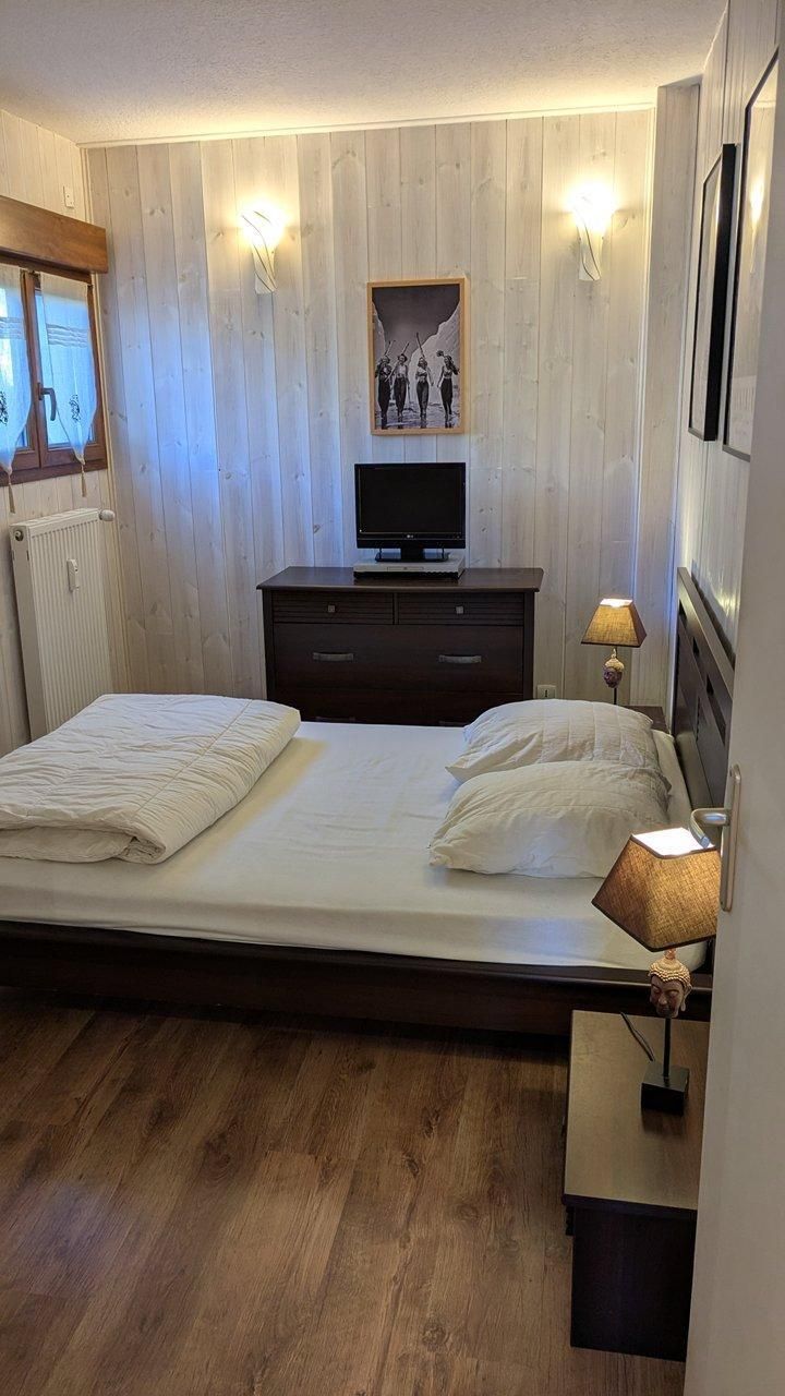 Une chambre à coucher comprenant un lit, une commode, un téléviseur et des lampes fixées au mur.