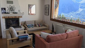 A living room with a fireplace, sofa, armchair, and a view of a mountainous landscape. - 100m from ski lifts, 2nd floor, balcony, tv, ski locker, 55m², Orcières Merlette 1850 (Orcières)