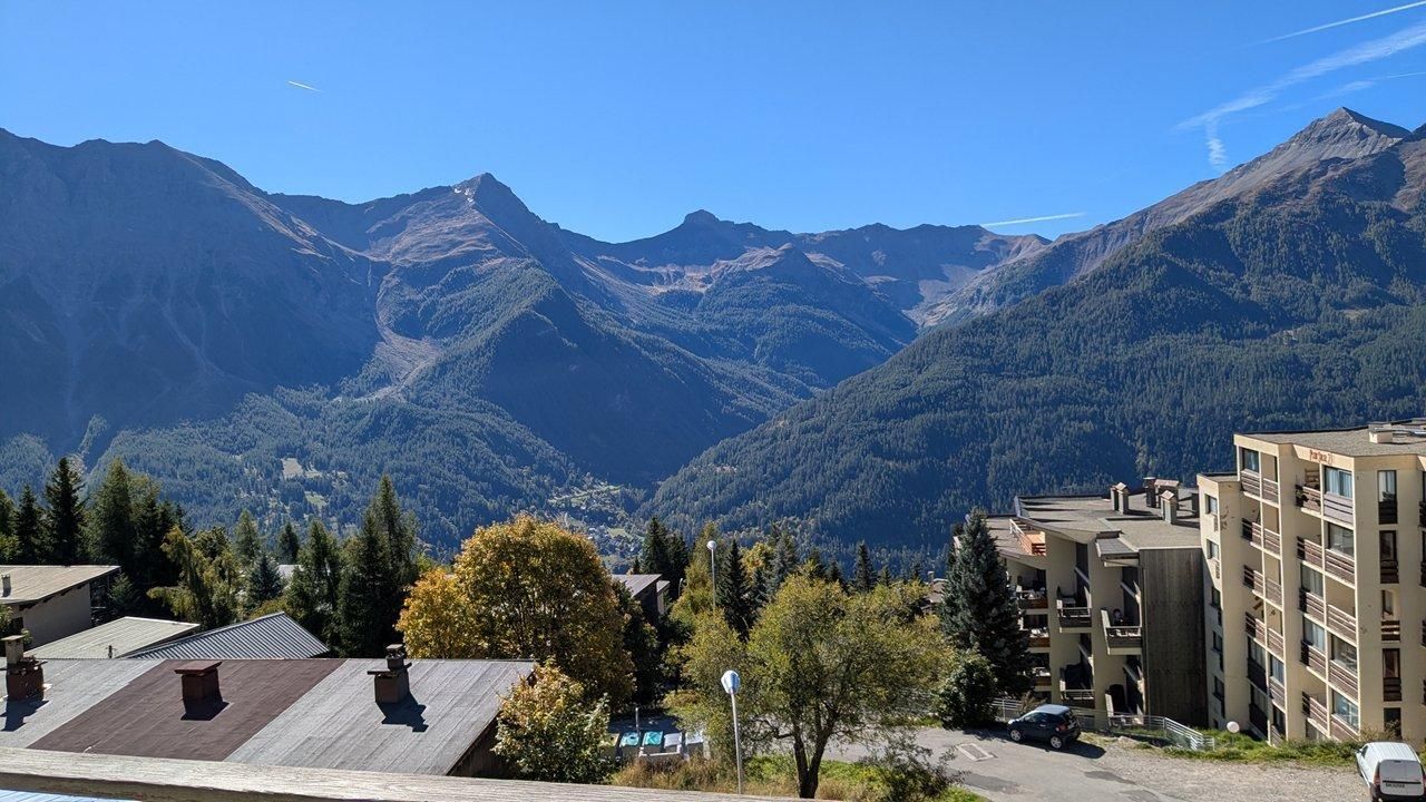 A mountain landscape with a building featuring multiple balconies and a parking area.