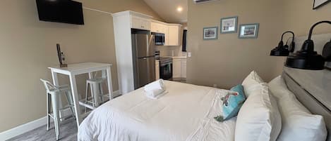 A hotel room with a bed, a desk, a chair, a ceiling fan, and a flat-screen TV.