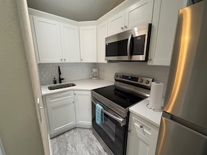 A kitchen with white cabinets, a stainless steel refrigerator, a microwave, an oven, and a coffee maker.