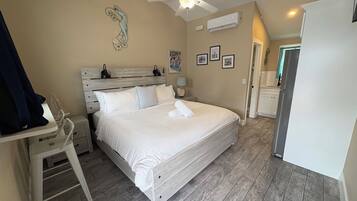 Une chambre à coucher comprenant un lit, un bureau, une chaise, un ventilateur de plafond et une porte donnant sur une autre pièce.