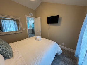 A hotel room with a bed, a television mounted on the wall, and a door leading to a bathroom.